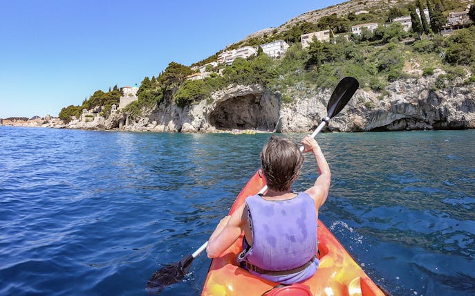 Kayaker paddling near rocky coastline in Dubrovnik during morning.