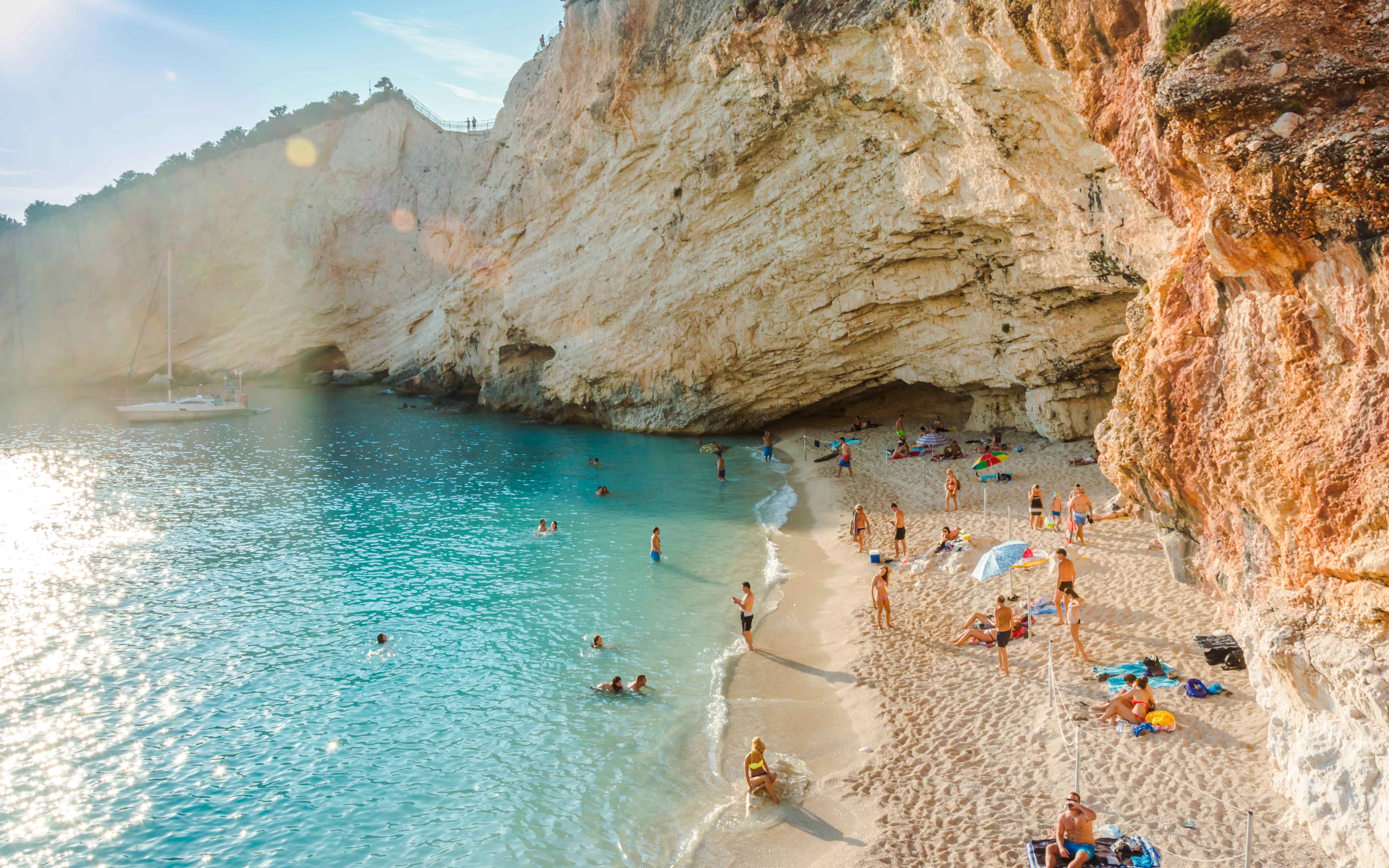 Beachgoers enjoying the sun and turquoise waters on a sandy beach in the Ionian Islands.