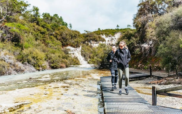 Visitors walking on a boardwalk at Wai-O-Tapu Thermal Wonderland, surrounded by geothermal landscape.