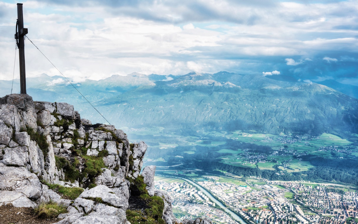 View from Nordkette mountain overlooking Innsbruck, Austria, with a summit cross in the foreground.