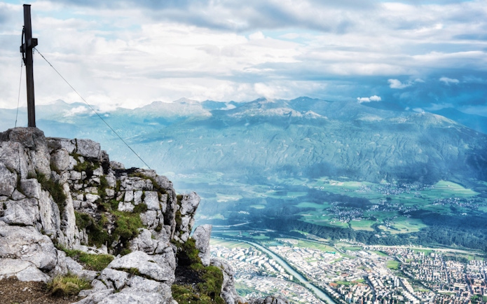 View from Nordkette mountain overlooking Innsbruck, Austria, with a summit cross in the foreground.