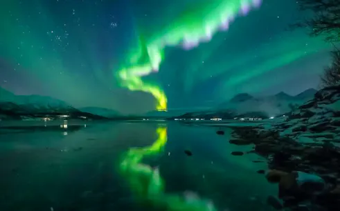 Northern lights over a tranquil lake during Northern Lights Chase tour from Tromso.