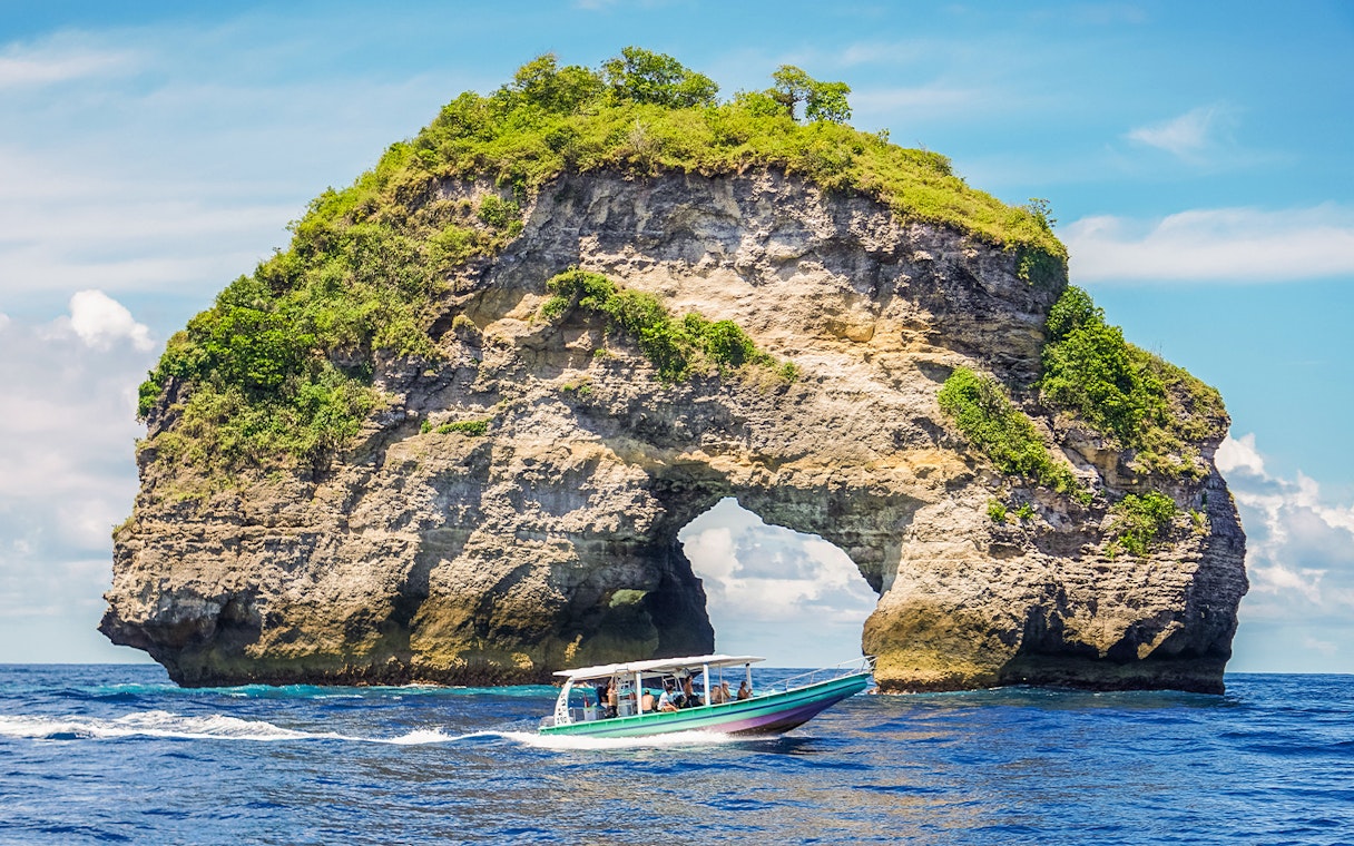 Speedboat with tourists approaching Nusa Penida Island, Bali, showcasing unique coastal views.