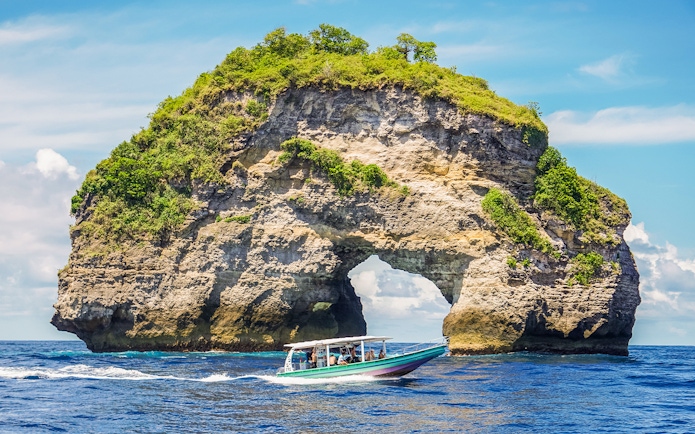 Speedboat with tourists approaching Nusa Penida Island, Bali, showcasing unique coastal views.