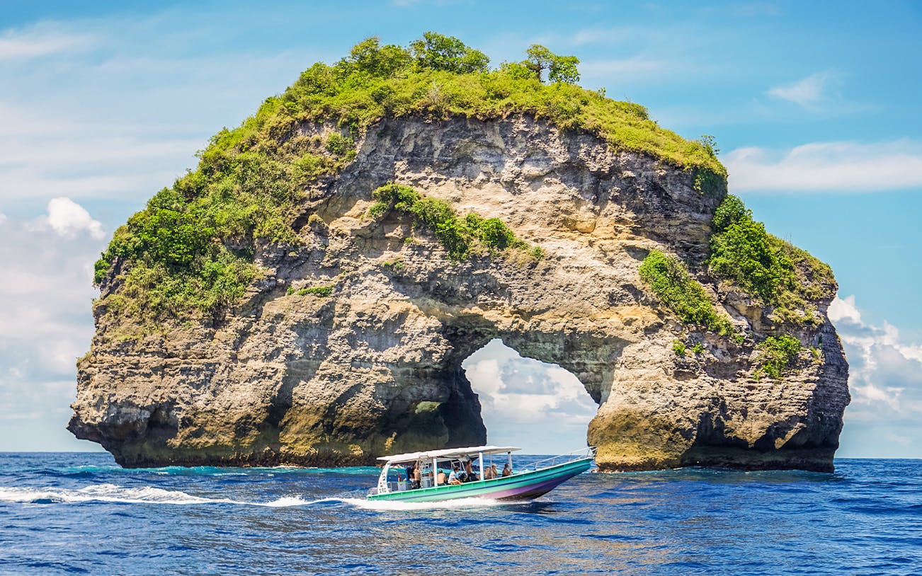 Speedboat with tourists approaching Nusa Penida Island, Bali, showcasing unique coastal views.