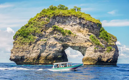 Speedboat with tourists approaching Nusa Penida Island, Bali, showcasing unique coastal views.