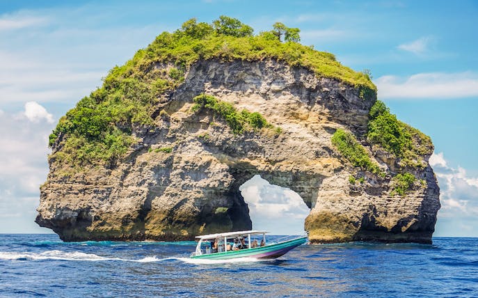Speedboat with tourists approaching Nusa Penida Island, Bali, showcasing unique coastal views.