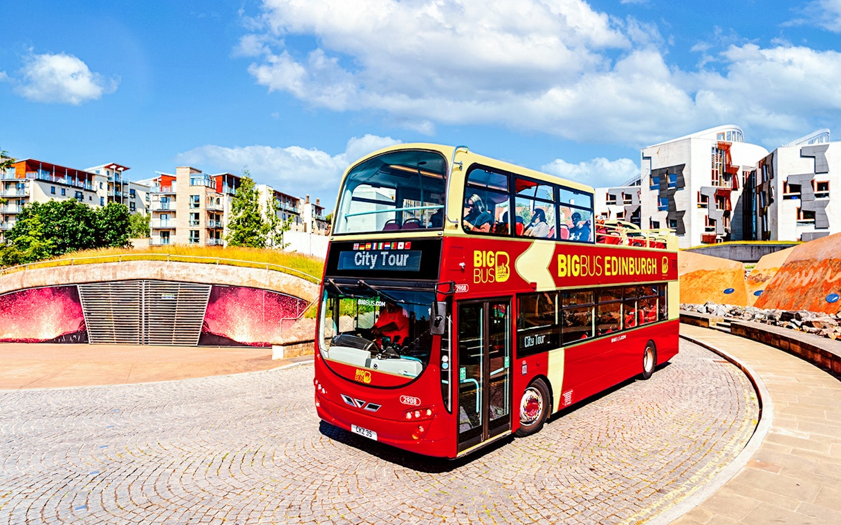 Edinburgh hop-on hop-off bus near modern architecture.