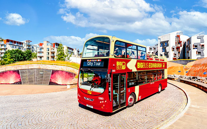 Edinburgh hop-on hop-off bus near modern architecture.