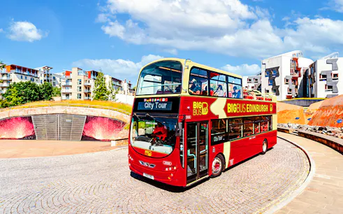 Edinburgh hop-on hop-off bus near modern architecture.