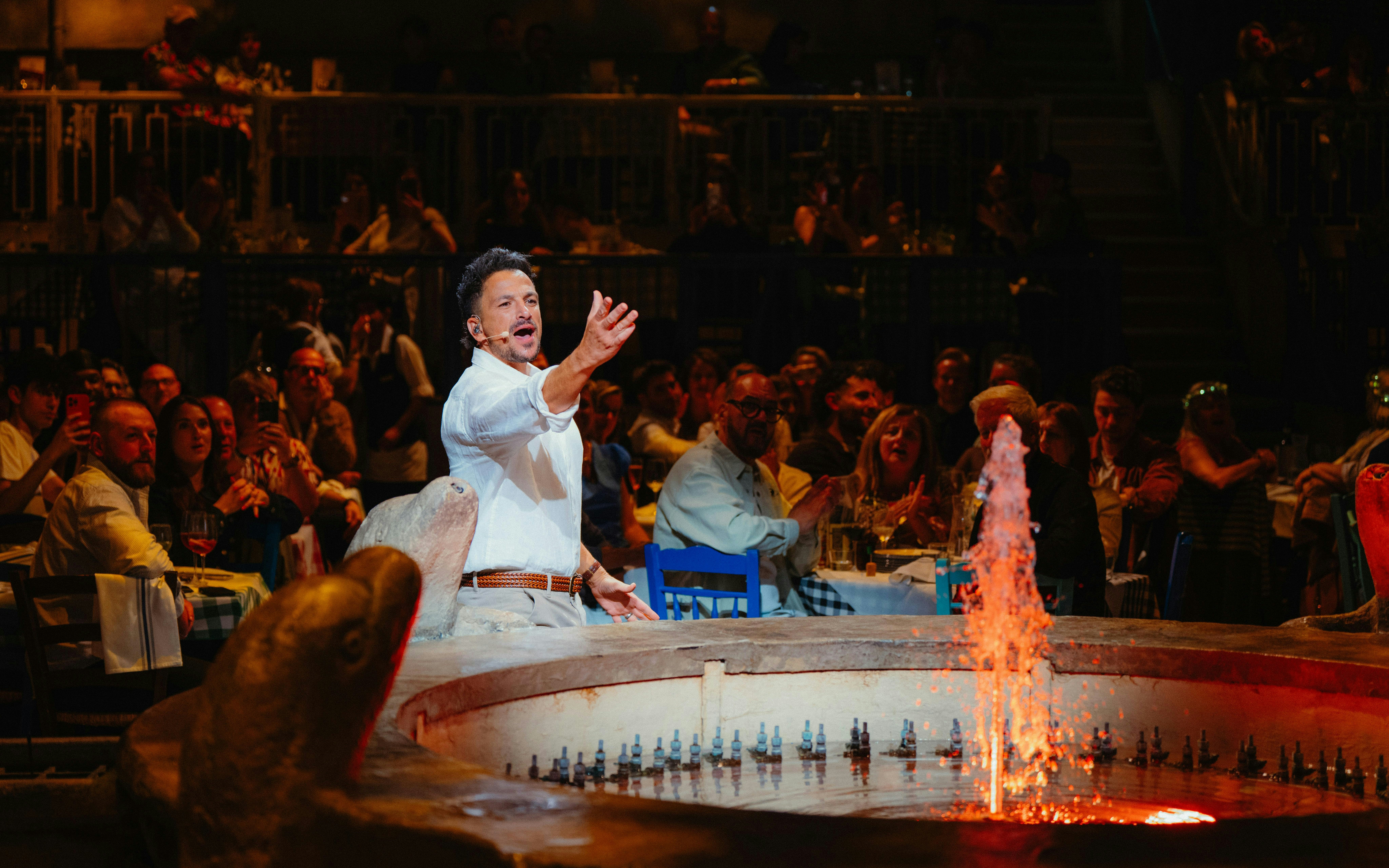Performer engaging audience at Mamma Mia! The Party with fountain in foreground.
