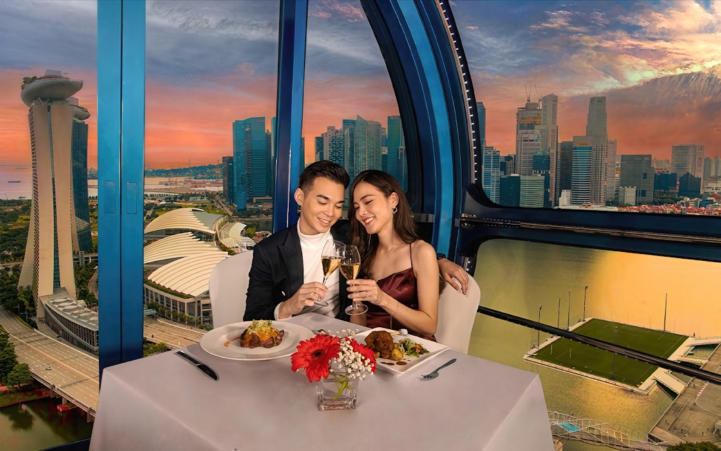Couple toasting champagne at sunset on Singapore Flyer with city skyline view.