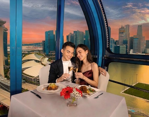 Couple toasting champagne at sunset on Singapore Flyer with city skyline view.