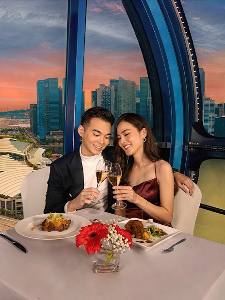 Couple toasting champagne at sunset on Singapore Flyer with city skyline view.