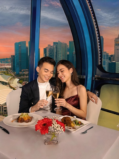 Couple toasting champagne at sunset on Singapore Flyer with city skyline view.