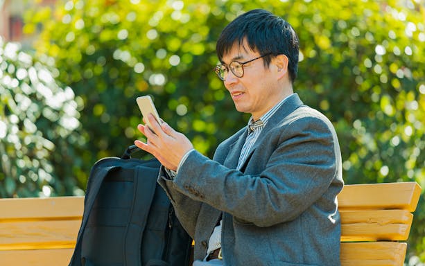 Man video calling on phone while sitting on a park bench.