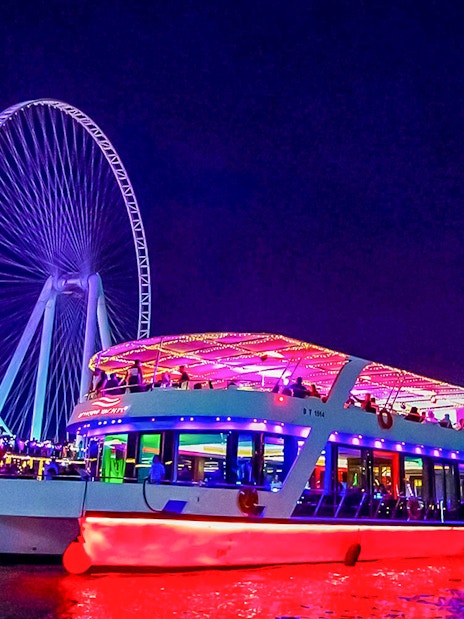 Dinner cruise with live music near illuminated Ferris wheel at night.