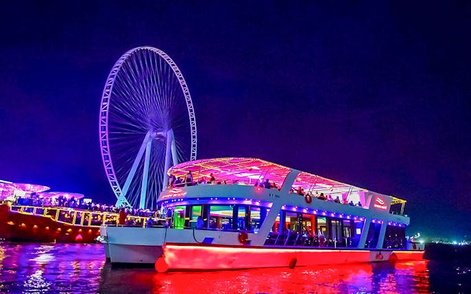 Dinner cruise with live music near illuminated Ferris wheel at night.