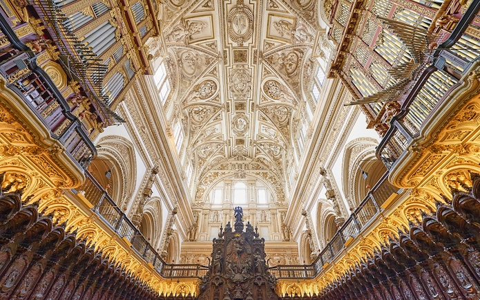 Nave and choir stalls with ornate ceiling and organ pipes in a historic cathedral.