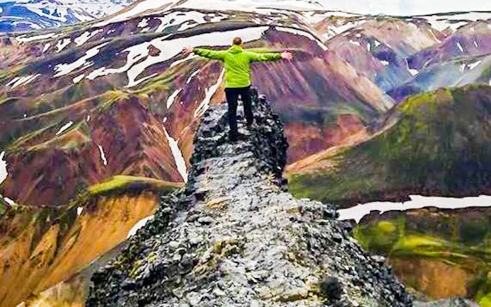 Hiker on rocky ridge in Landmannalaugar Highlands, Iceland, with colorful mountains in background.