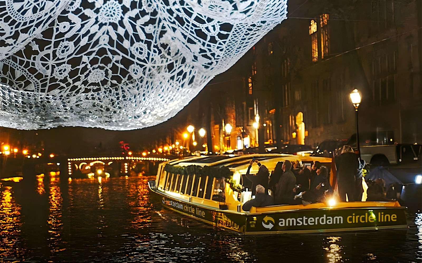Cruise boat under illuminated lace artwork during Amsterdam Light Festival.