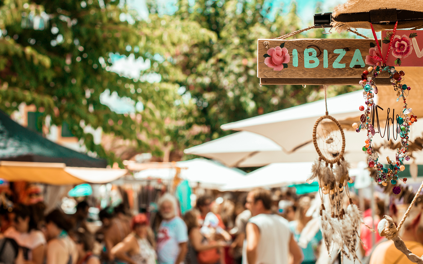 Market outside in Ibiza with a wooden sing that says ibiza on a sunny day
