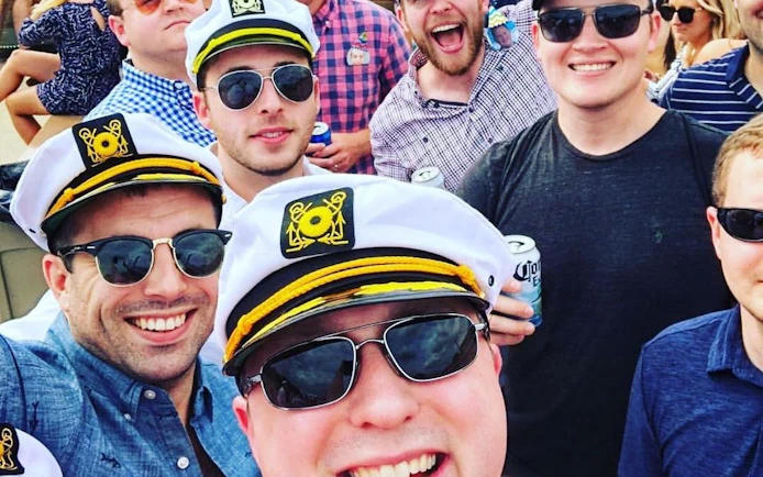 Group enjoying Washington, DC yacht cruise with captain hats and drinks.