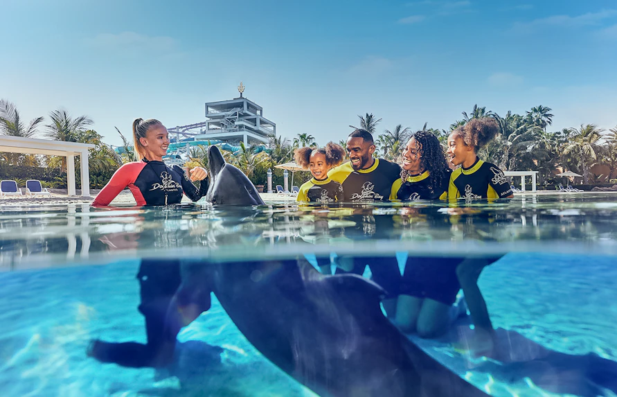 Family interacting with a dolphin at Aquaventure Waterpark, Dubai.
