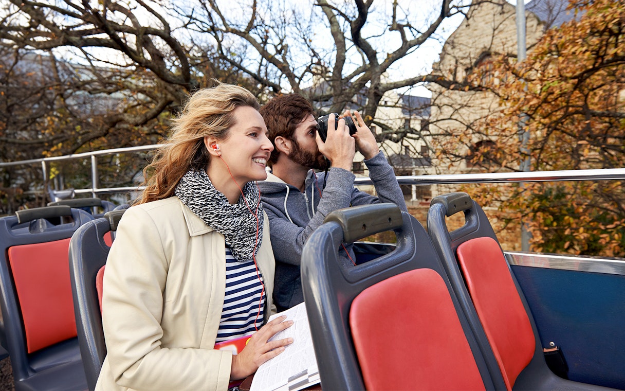 Couple enjoying audio guide on open-top tour bus.