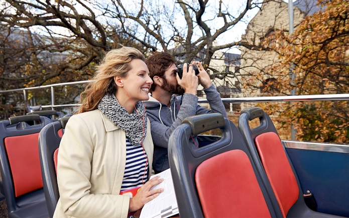 Couple enjoying audio guide on open-top tour bus.