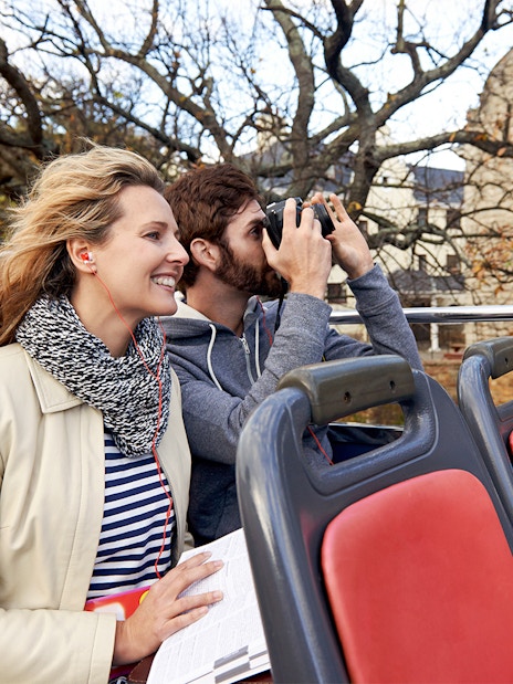 Couple enjoying audio guide on open-top tour bus.