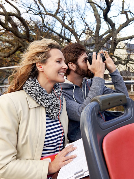 Couple enjoying audio guide on open-top tour bus.