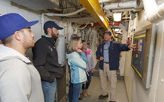 Guided tour group in engineering facility with guide explaining control panel.