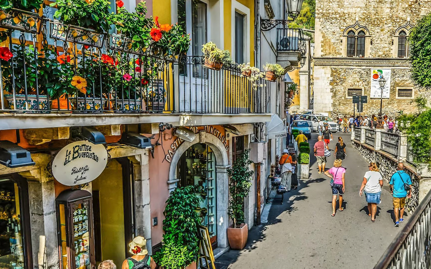 Narrow alleyway in Taormina with colorful flowers and people walking.
