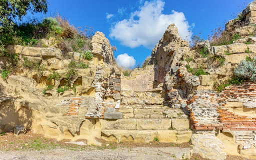 Ancient stone ruins at the Archaeological Park of Cumae under a blue sky.