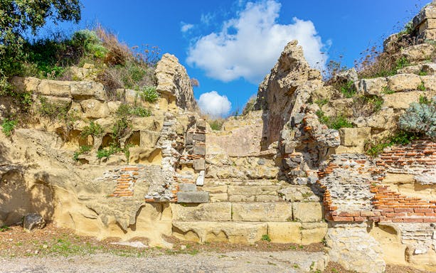 Ancient stone ruins at the Archaeological Park of Cumae under a blue sky.