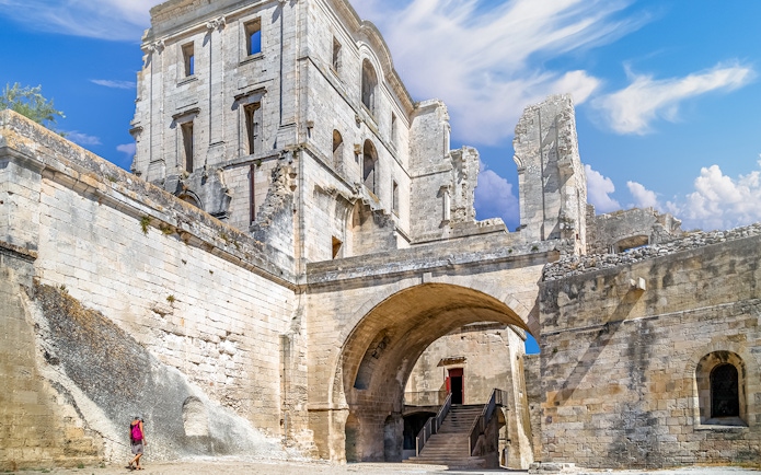 Montmajour Abbey ruins with archway and visitor in Arles, France.