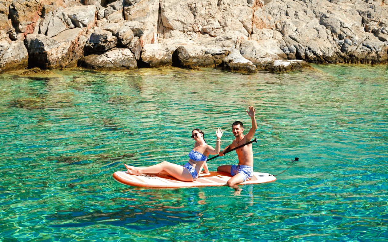 Couple paddleboarding near rocky shore on Dia Island during catamaran day cruise.