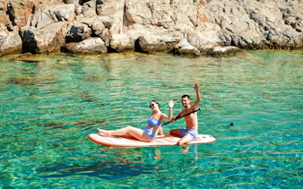 Couple paddleboarding near rocky shore on Dia Island during catamaran day cruise.