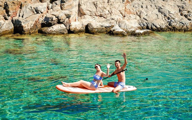 Couple paddleboarding near rocky shore on Dia Island during catamaran day cruise.