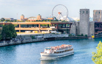 Chicago River cruise boat with tourists, Ferris wheel and cityscape in background.
