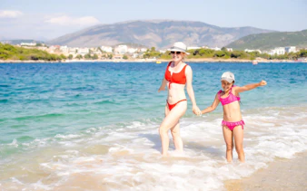 Guests enjoying the beach near Ksamil, Albania, with mountains in the background.