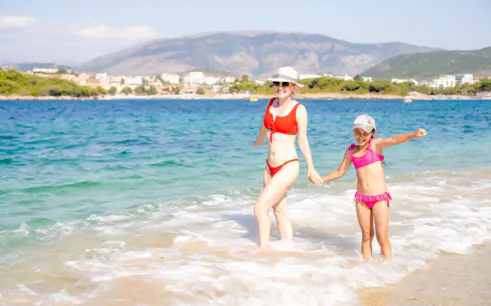 Guests enjoying the beach near Ksamil, Albania, with mountains in the background.