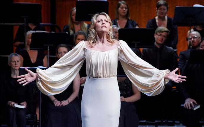 Performer in white gown during Theodora concert with choir in background.