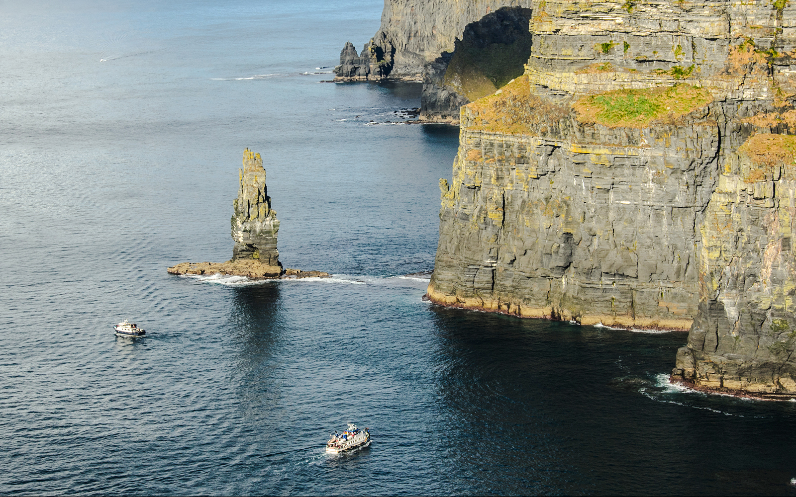 Tour boats near the Cliffs of Moher, Ireland, with a sea stack in view.
