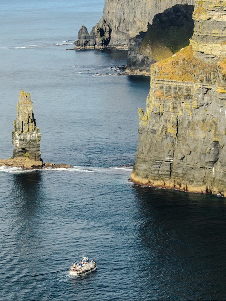 Tour boats near the Cliffs of Moher, Ireland, with a sea stack in view.