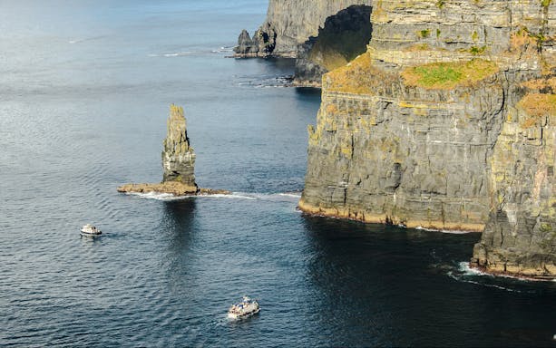 Tour boats near the Cliffs of Moher, Ireland, with a sea stack in view.