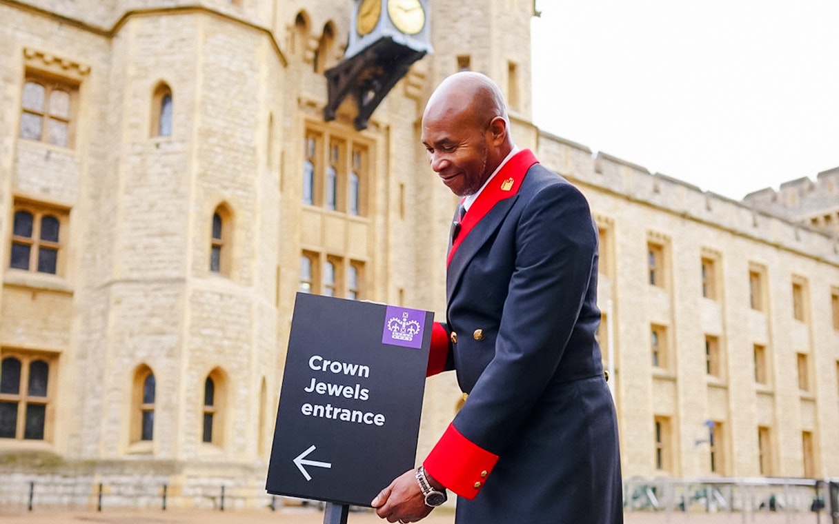Crown Jewels entrance sign at the Tower of London with a uniformed guard nearby.