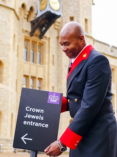 Crown Jewels entrance sign at the Tower of London with a uniformed guard nearby.