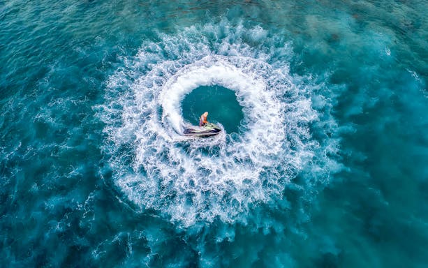 Jet ski creating circular waves in Pattaya's turquoise waters during island day trip.